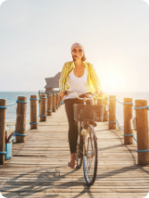 Frau fährt bei Sonnenuntergang mit dem Fahrrad über einen Holzsteg am Meer